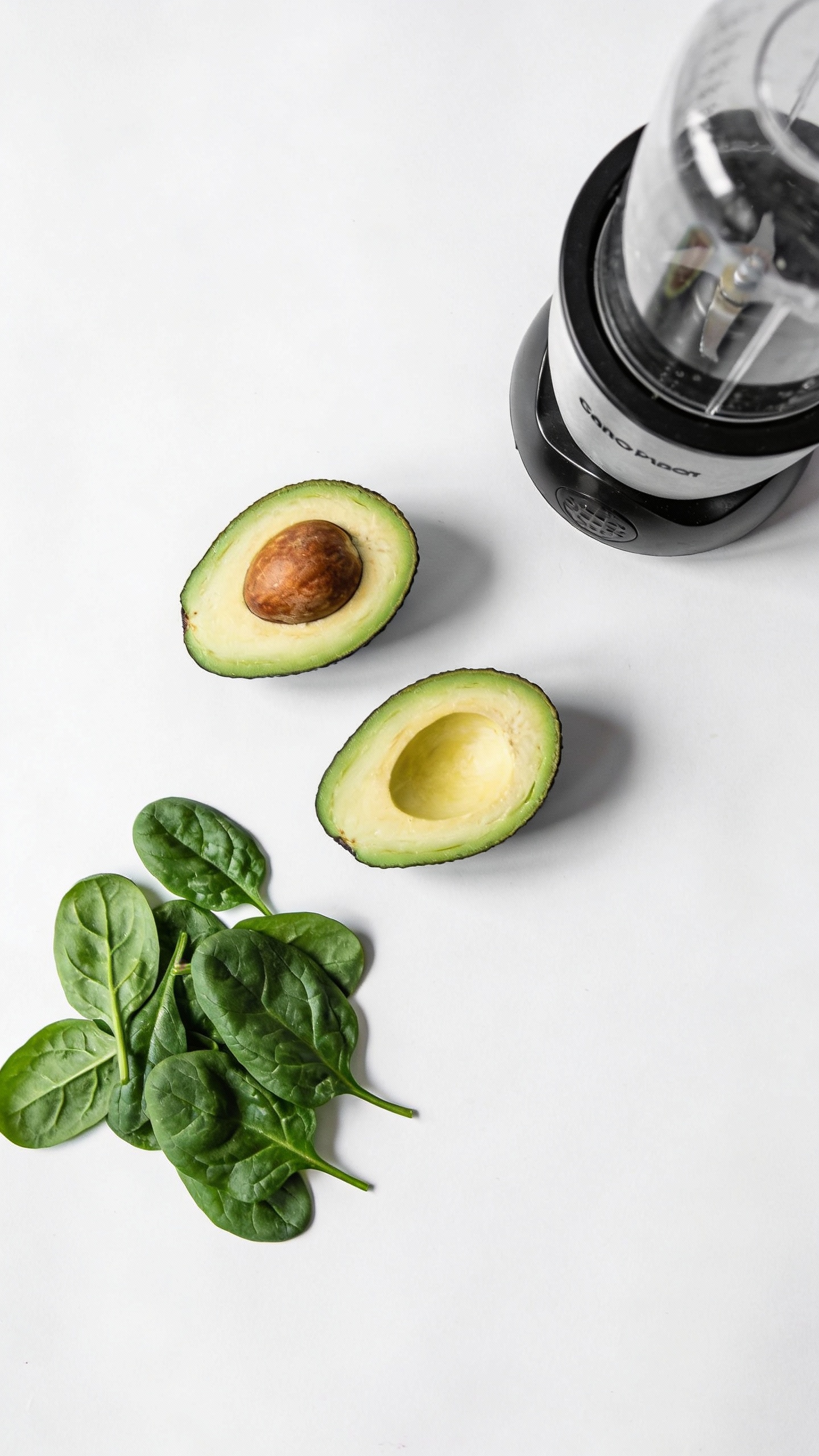 Overhead avocado halves, fresh spinach, blender, minimal white backdrop