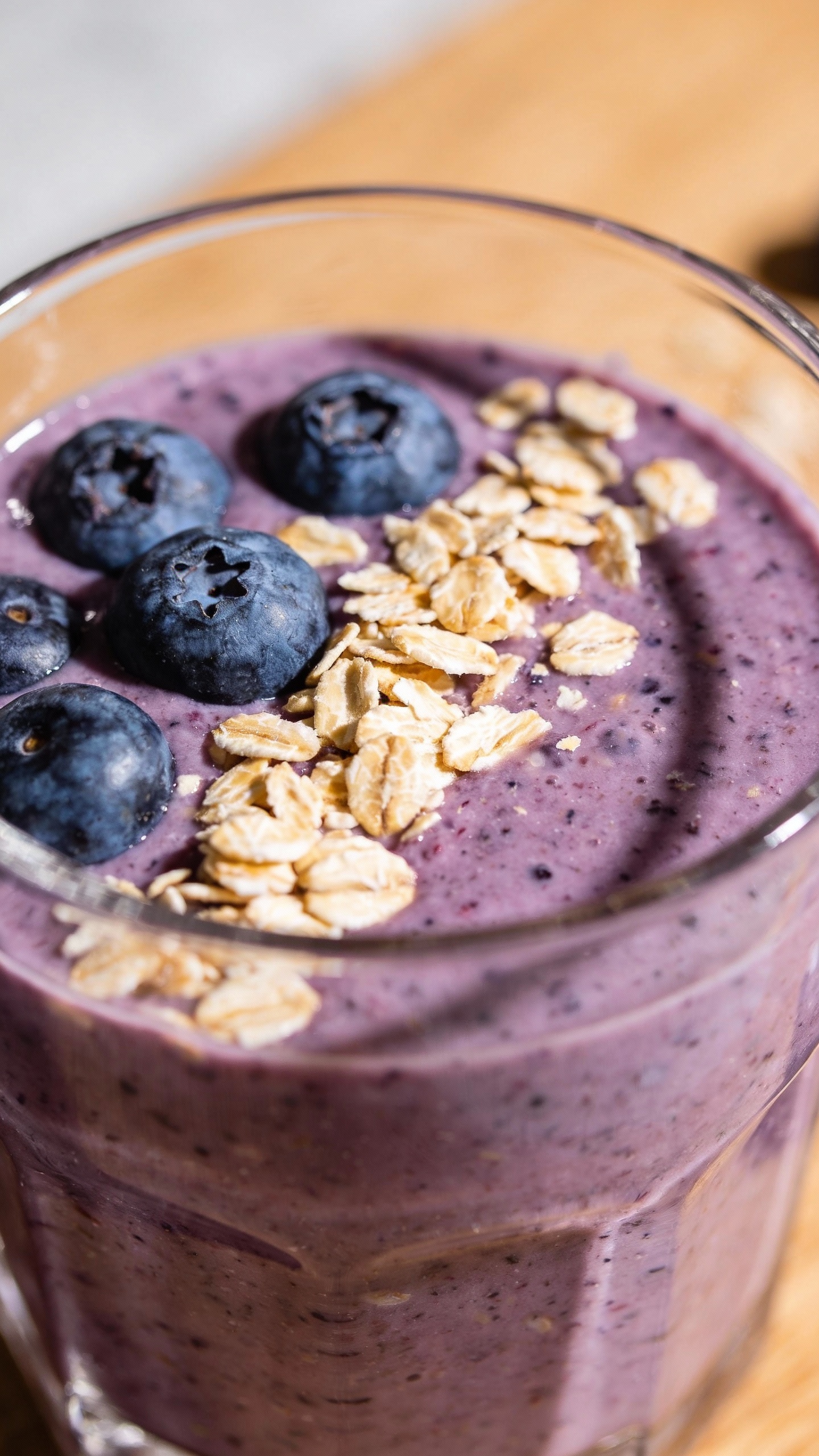 blueberry oat smoothie in clear glass, oats and berries garnish